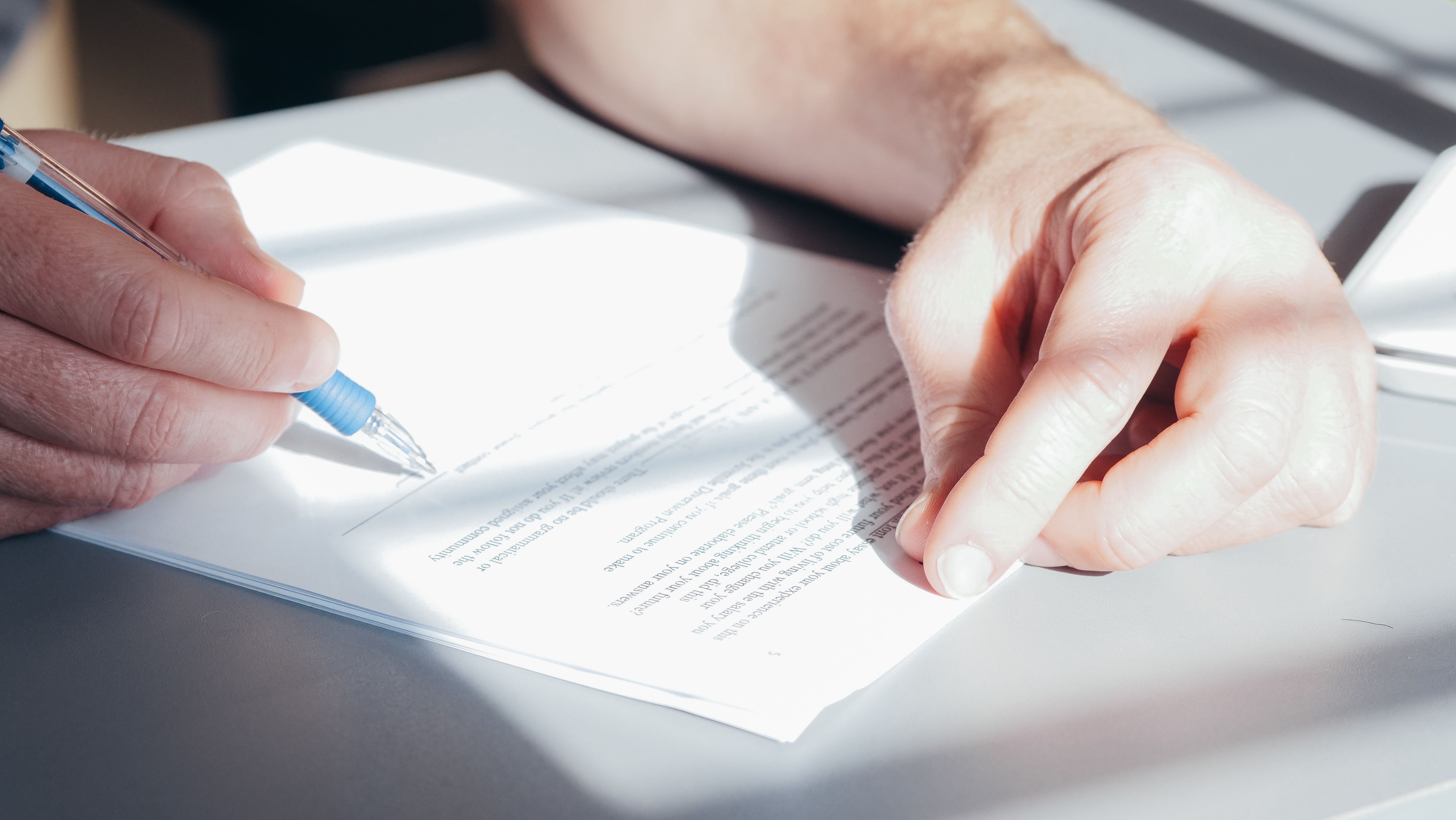 Close-up of hands signing a contract with a blue pen