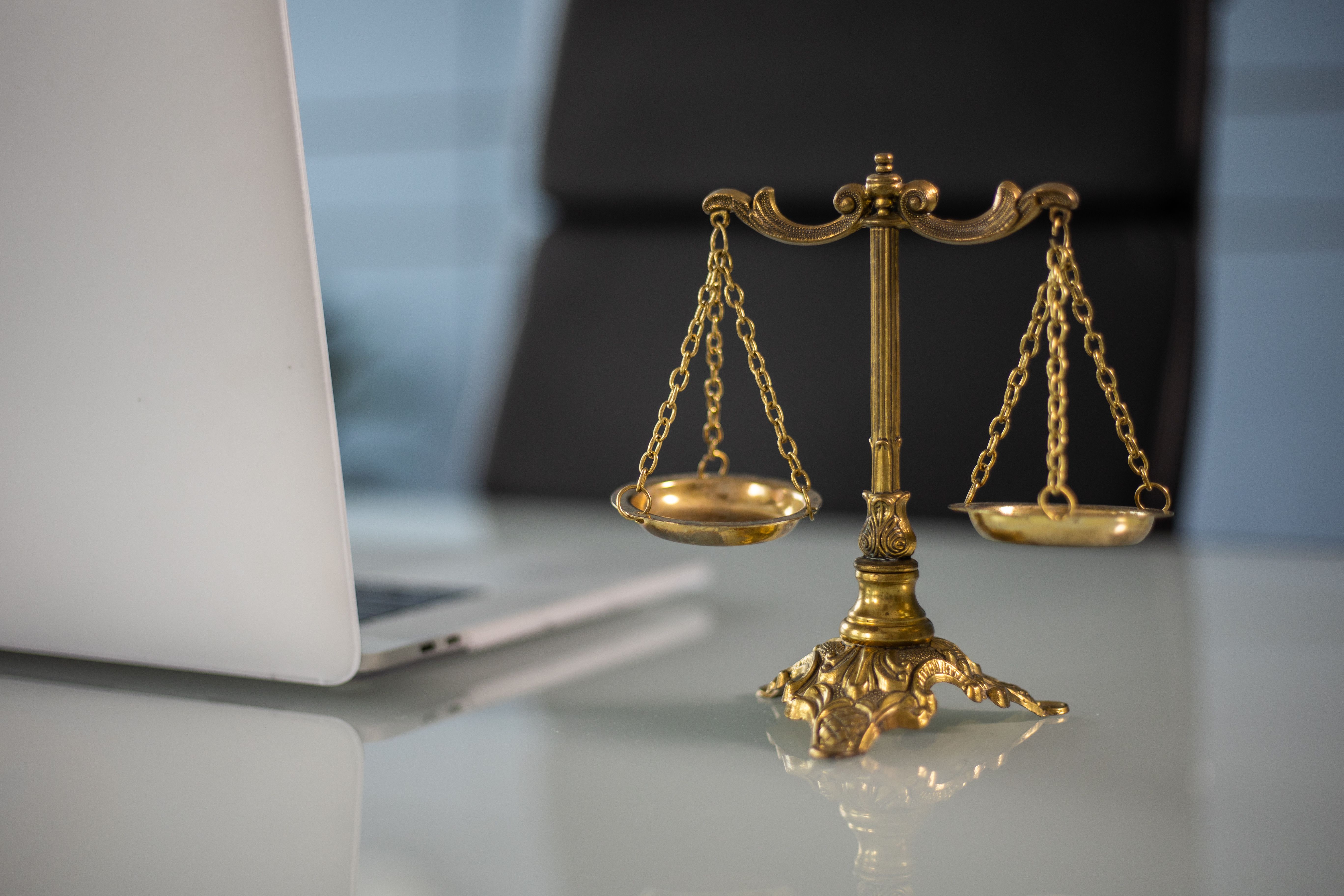 Golden justice scales on a desk beside a laptop