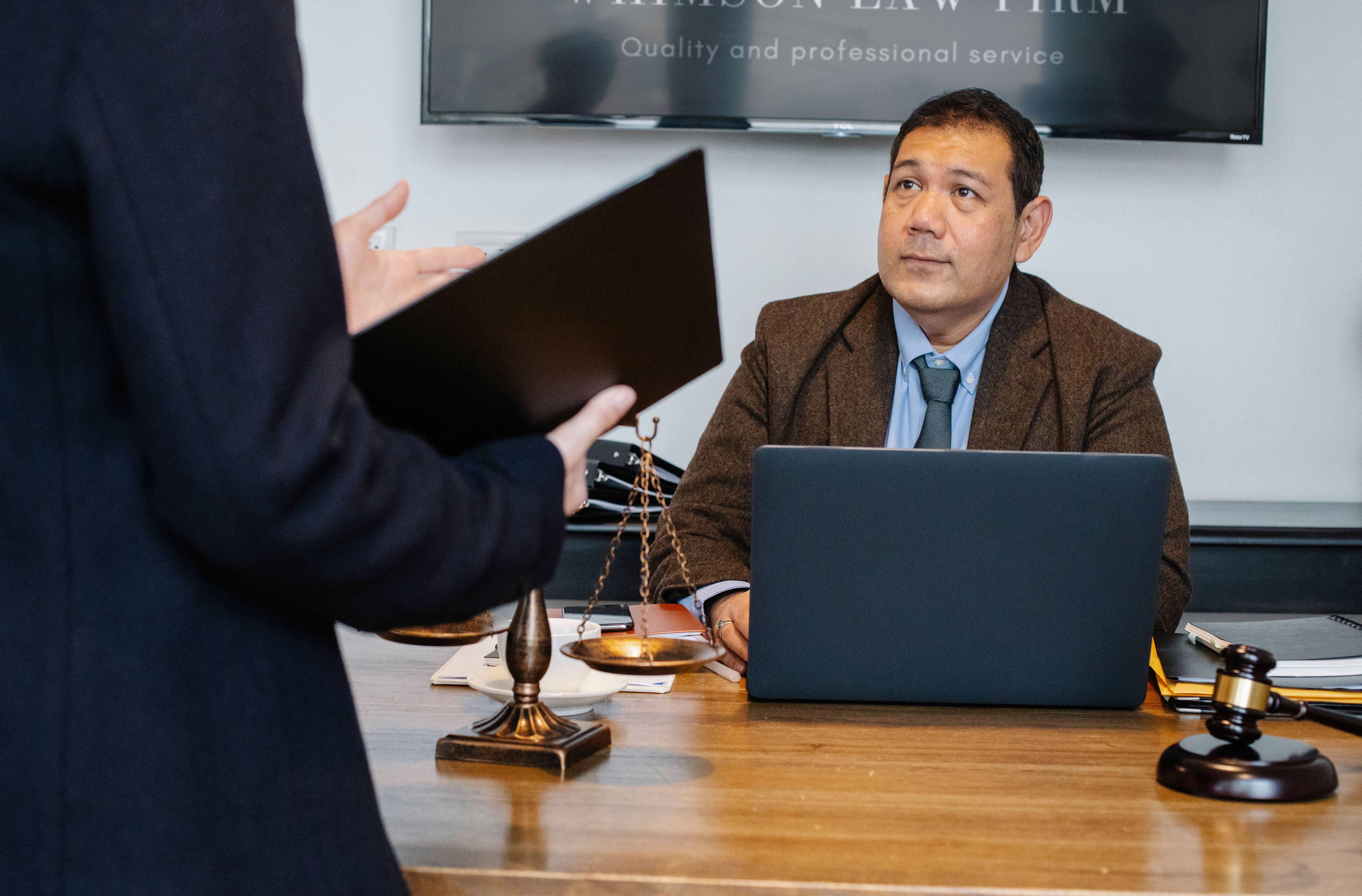 Lawyers reviewing case details with a laptop, gavel, and scales of justice during a legal consultation.