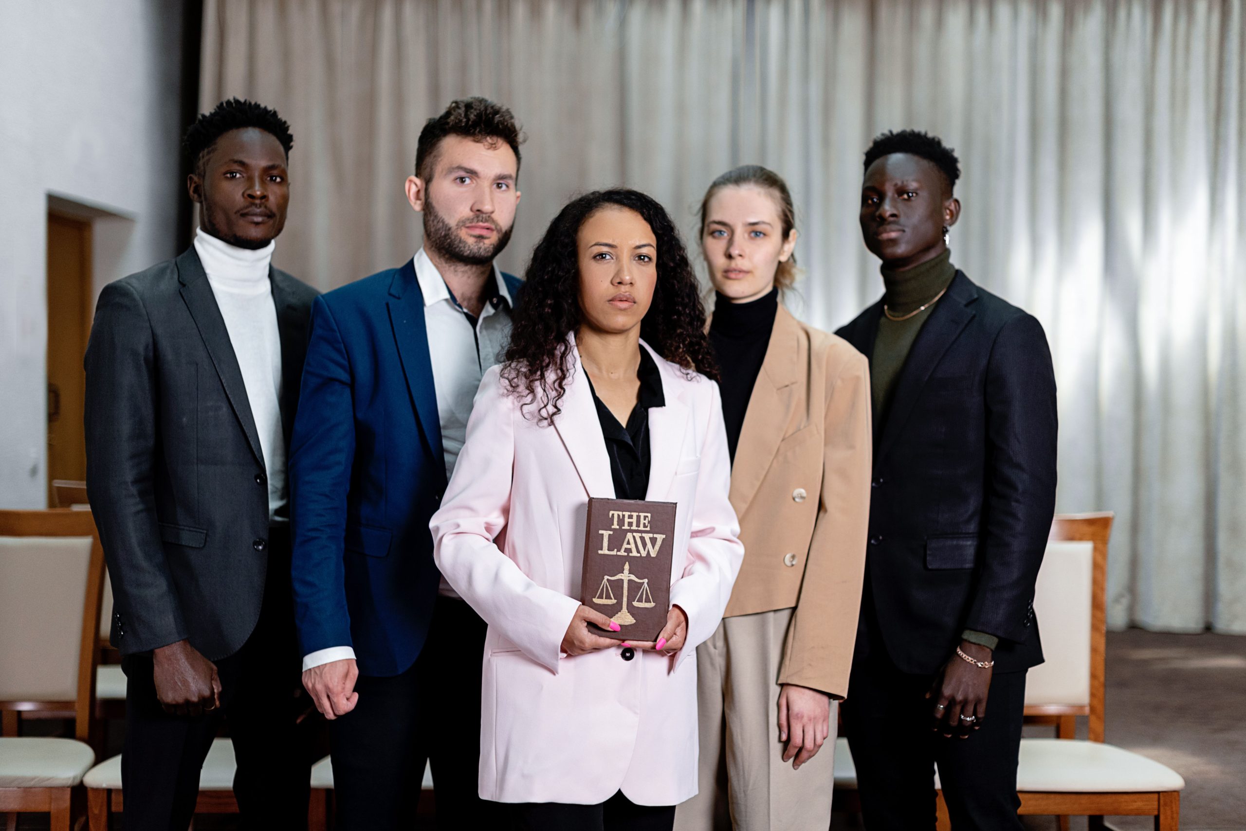 A diverse legal team standing together with a law book in a professional office, illustrating coordinated representation in a large-scale case.